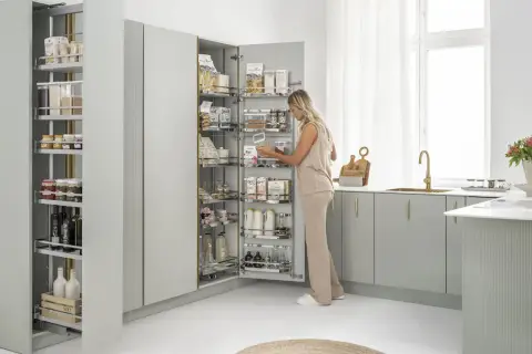 Kobieta wybiera produkty z wysokiej szafy z systemem szuflad, idealnej do przechowywania pokrywek i przetworów.